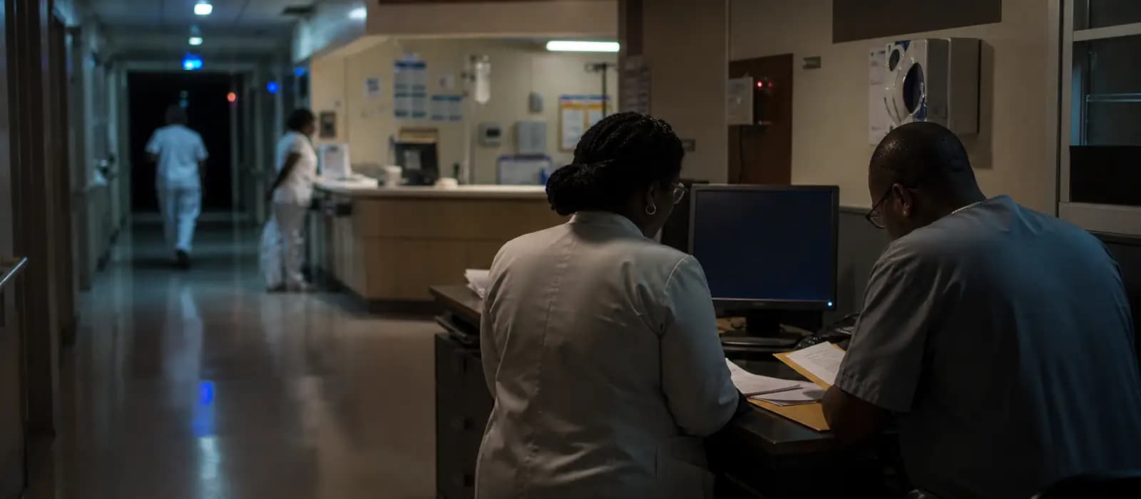 Couloir d'hôpital ouest-africain avec poste informatique et procédures papier en mode dégradé.